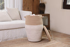 Tall jute and white woven basket storing blankets next to a living room sofa