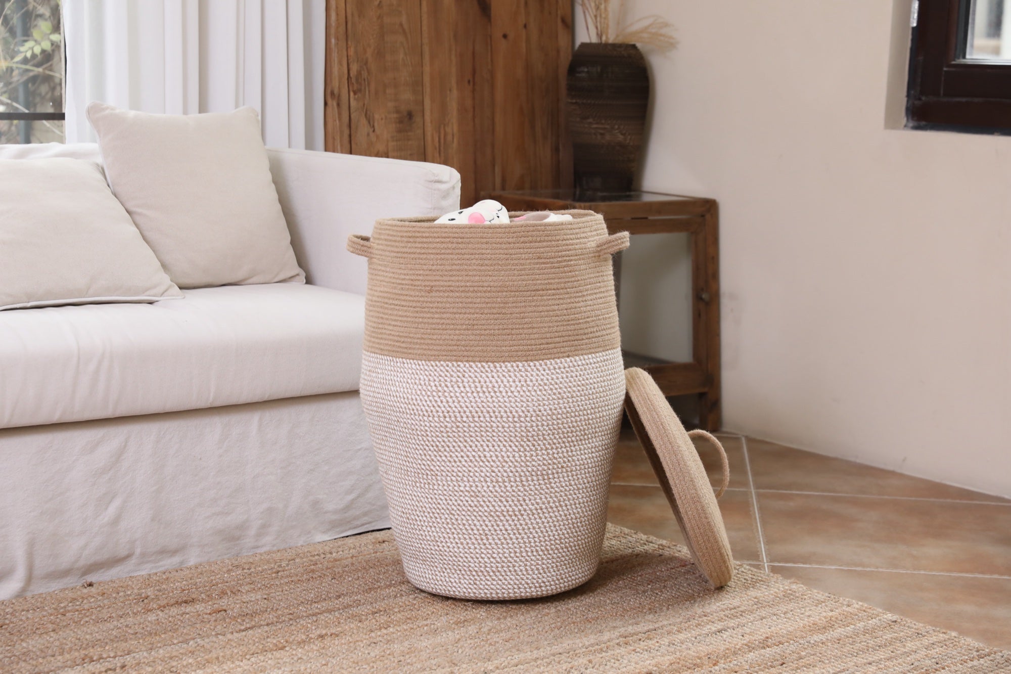 Tall jute and white woven basket storing blankets next to a living room sofa