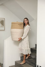 Woman carrying the jute and white tall laundry basket by its woven handles